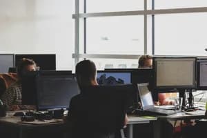 Zespół specjalistów IT współpracujący w nowoczesnym biurze software house'u przy biurkach z komputerami, analizujący makiety stron internetowych i kod.